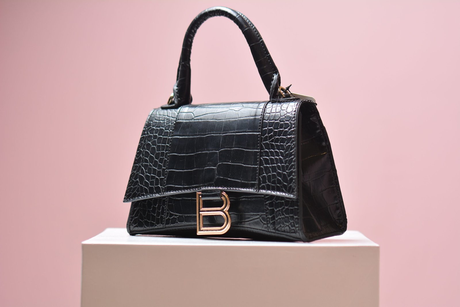 Elegant black leather handbag with textured design on a pink background, perfect for high-end fashion shoots.